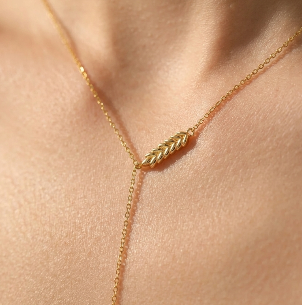 Gold necklace with a leaf-shaped pendant on a person's neck