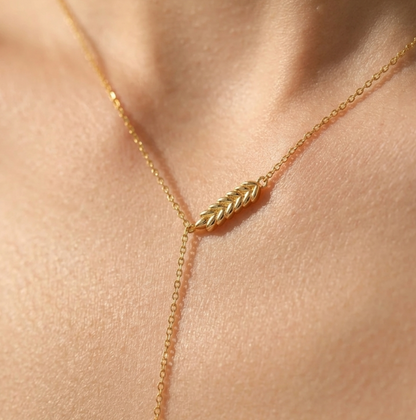 Gold necklace with a leaf-shaped pendant on a person's neck