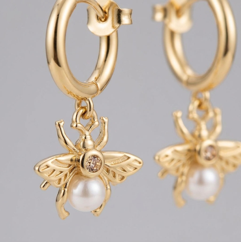 Gold hoop earrings with bee charms and pearls on a gray background