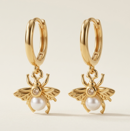Gold plated sterling silver bee-shaped earrings with faux pearl centers on a beige background