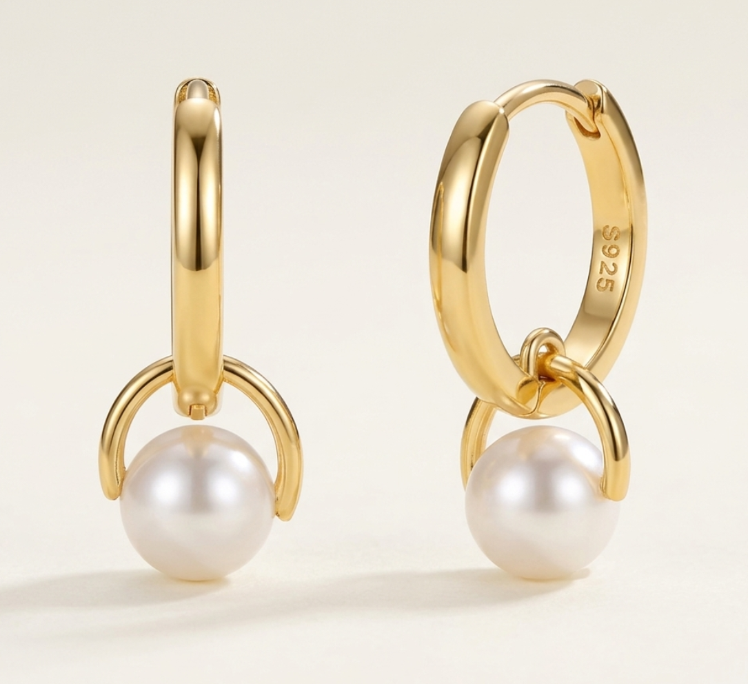 Gold plated sterling silver hoop earrings with pearl drops on a light beige background