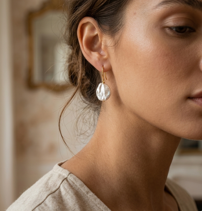 Close-up of a woman wearing a gold earring with a irregular shaped freshwater pearl.