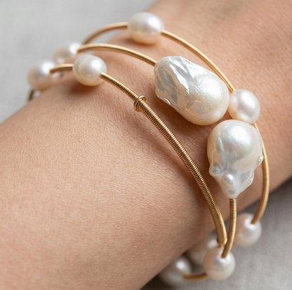 Gold bracelet with pearls on a wrist against a neutral background