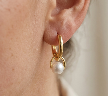 Gold hoop earring with a pearl drop worn by a person.