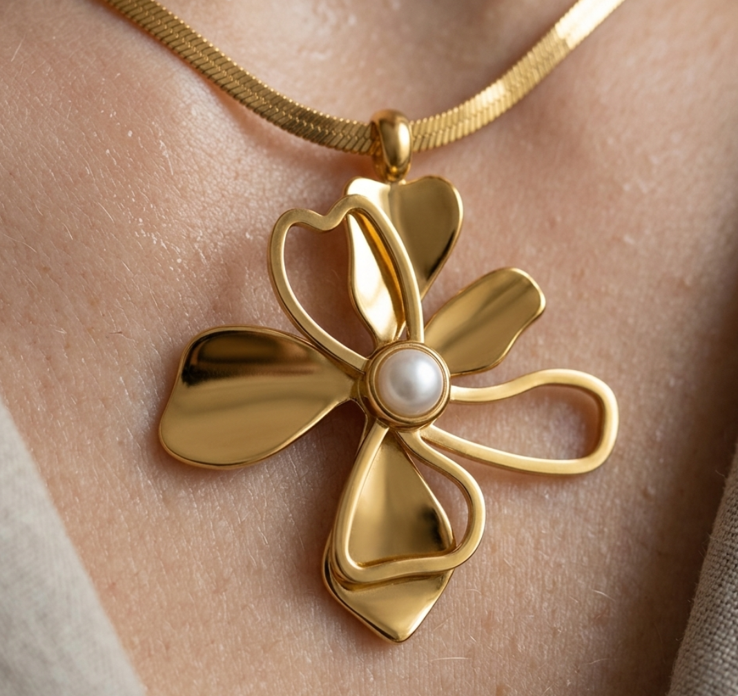 Gold necklace with a floral pendant featuring a pearl on a person's neck.