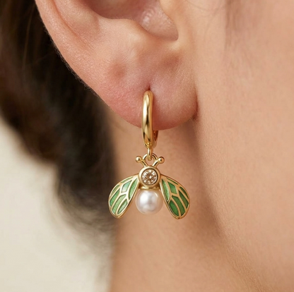 Gold earring with green accents and a pearl on an ear against a neutral background
