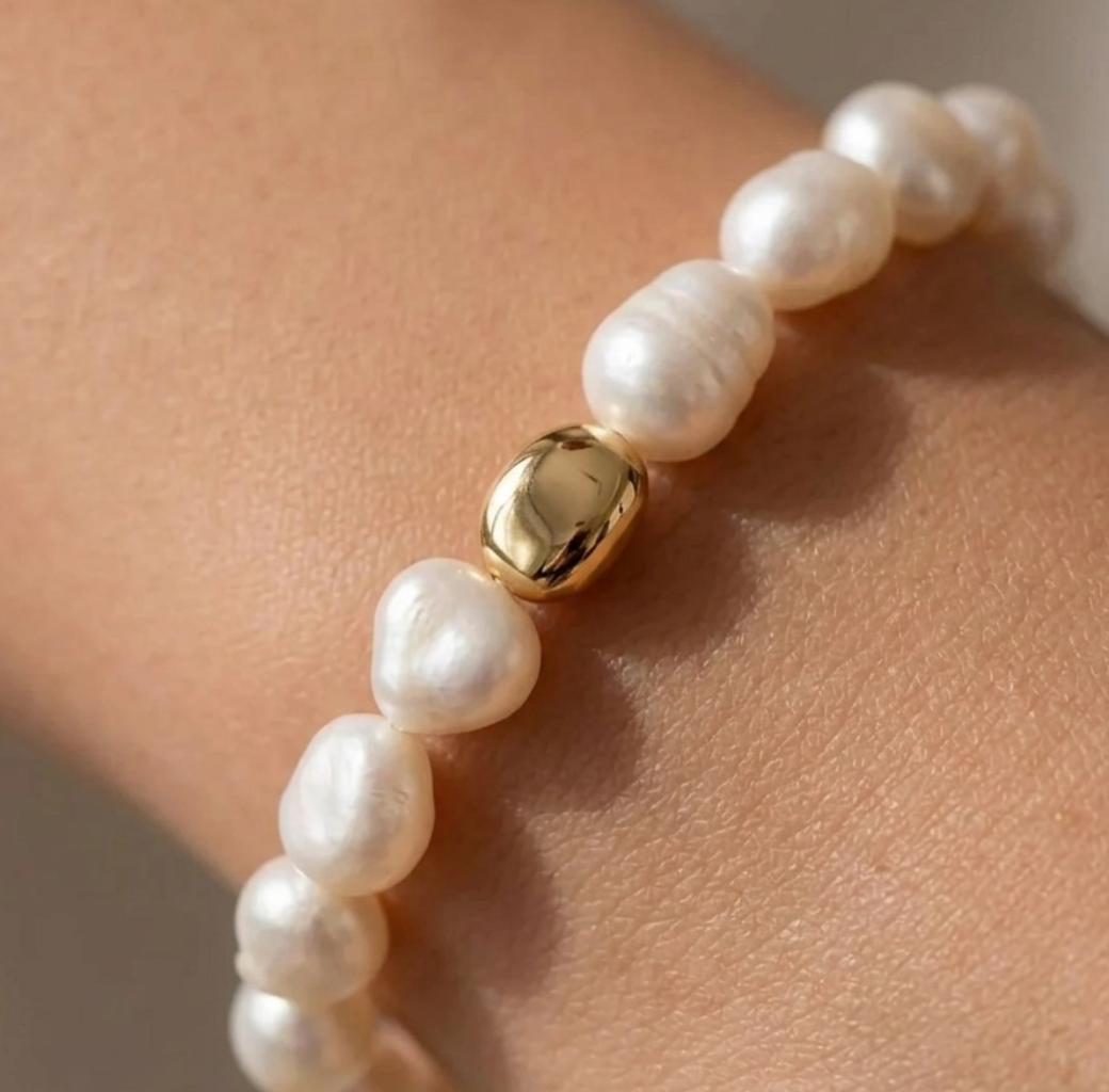 Pearl bracelet with a gold bead on a wrist against a neutral background