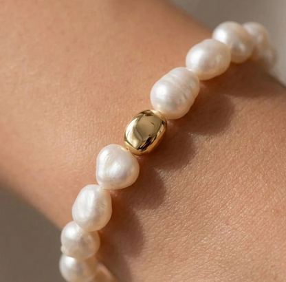 Pearl bracelet with a gold bead on a wrist against a neutral background