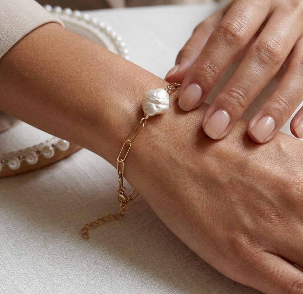 Close-up of a hand wearing a gold bracelet with a pearl charm on a light background