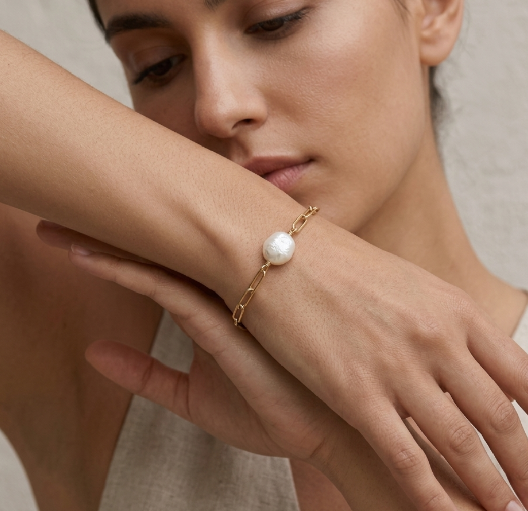 Woman wearing a gold bracelet with a pearl on a neutral background