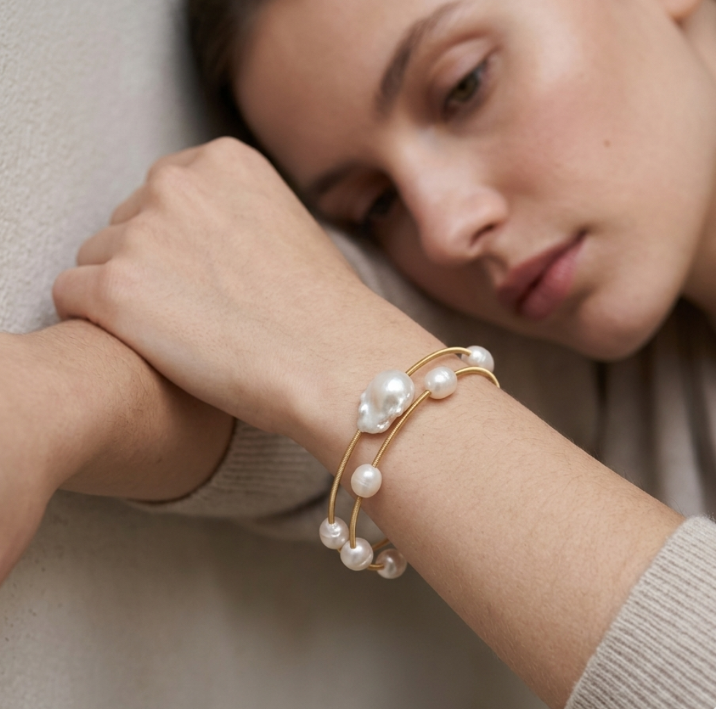 Woman wearing a gold bracelet with pearls on a neutral background
