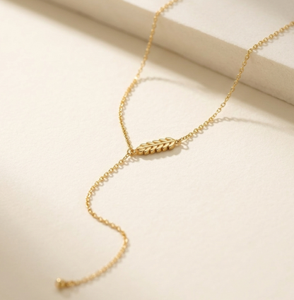 Veruccia Gold necklace with a leaf-shaped pendant on a light beige background