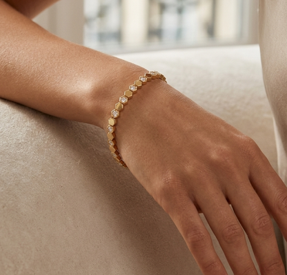 Close-up of a hand wearing a gold bracelet on a neutral background